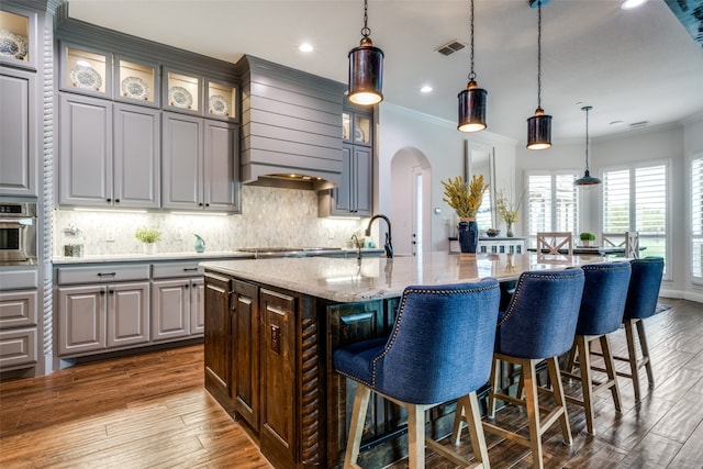 kitchen featuring a center island with sink, pendant lighting, gray cabinetry, and hardwood / wood-style flooring