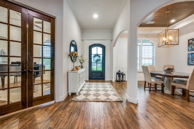 foyer entrance with french doors, crown molding, wood-type flooring, wooden ceiling, and a notable chandelier