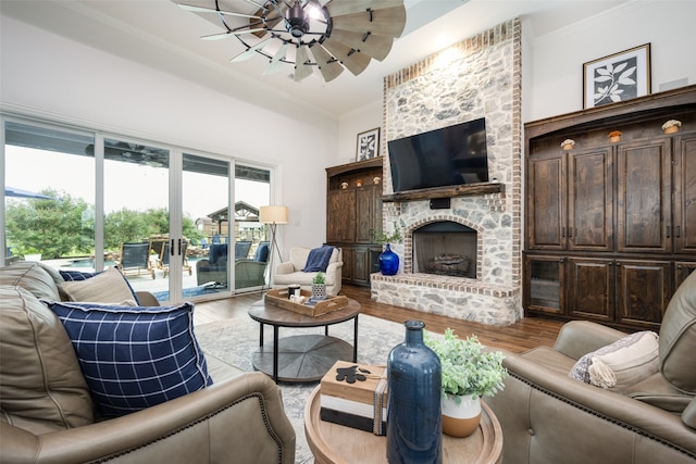 living room featuring hardwood / wood-style floors, ceiling fan, a stone fireplace, and ornamental molding