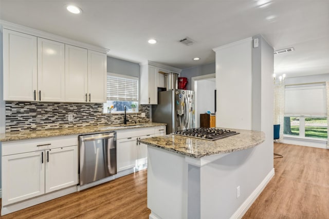 kitchen with appliances with stainless steel finishes, white cabinetry, light stone countertops, and sink