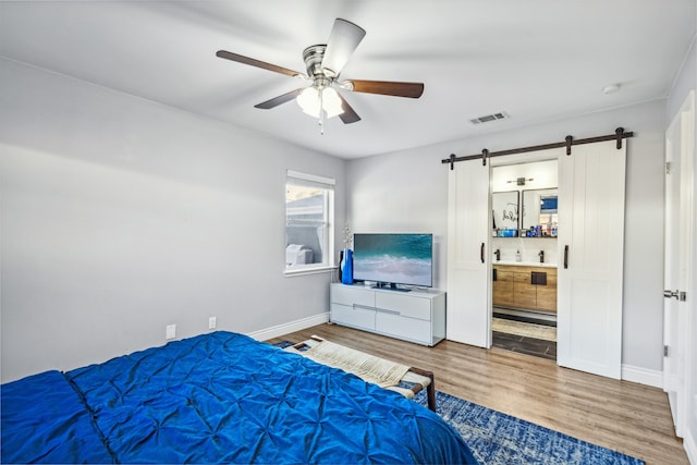 bedroom featuring hardwood / wood-style flooring, ceiling fan, a barn door, and ensuite bath