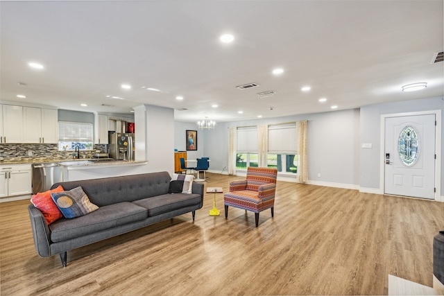 living room featuring a chandelier, light wood-type flooring, a wealth of natural light, and sink