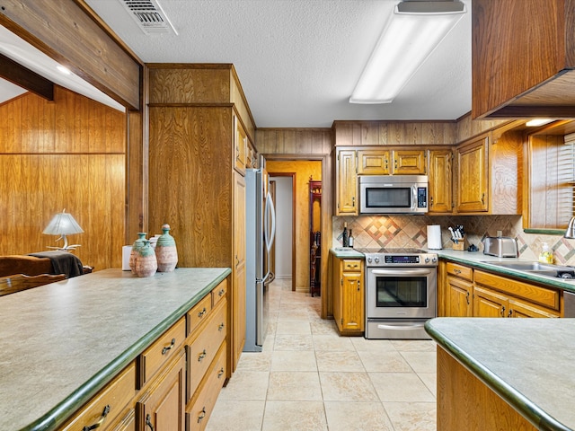 kitchen featuring appliances with stainless steel finishes, backsplash, beam ceiling, wood walls, and light tile patterned flooring