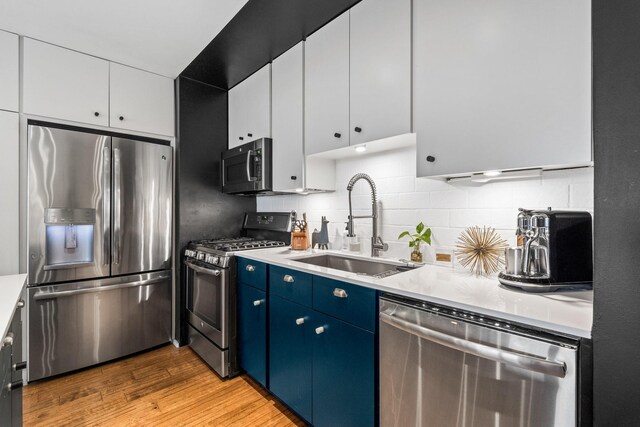 kitchen featuring sink, light wood-type flooring, blue cabinetry, appliances with stainless steel finishes, and white cabinetry