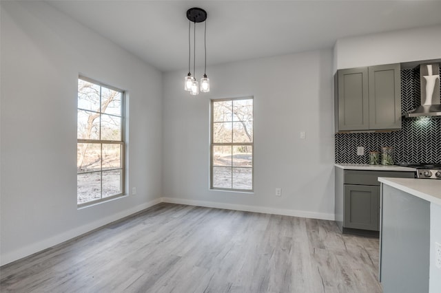 kitchen featuring light hardwood / wood-style floors, gray cabinets, hanging light fixtures, and wall chimney range hood