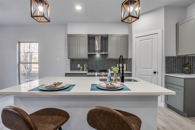 kitchen featuring gray cabinetry, a kitchen island with sink, decorative light fixtures, and wall chimney range hood