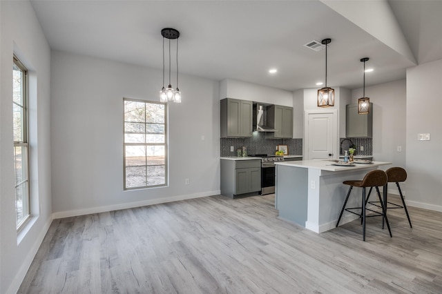 kitchen with a breakfast bar, wall chimney range hood, light countertops, gray cabinetry, and stainless steel range oven