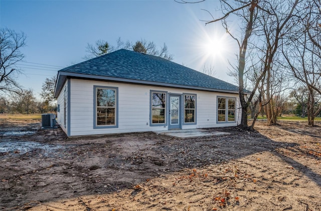 rear view of property with a shingled roof, cooling unit, and a patio