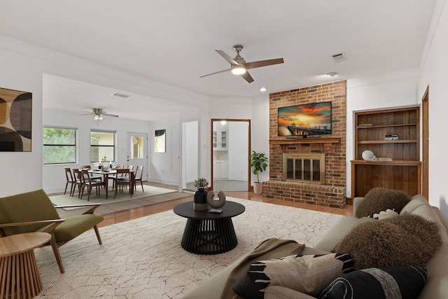 living room with ceiling fan, crown molding, light hardwood / wood-style floors, and a brick fireplace