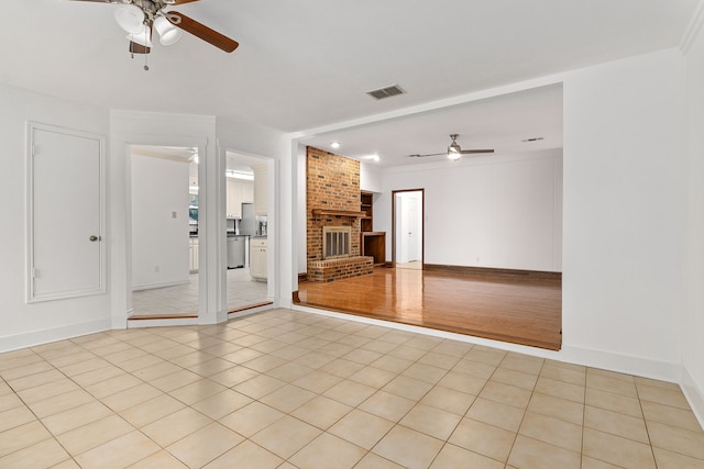 unfurnished living room with a brick fireplace, ceiling fan, ornamental molding, and light tile patterned flooring