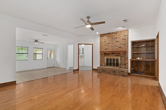 unfurnished living room with a brick fireplace, ceiling fan, crown molding, and light hardwood / wood-style flooring