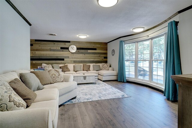 living room featuring hardwood / wood-style flooring, wood walls, crown molding, and a textured ceiling