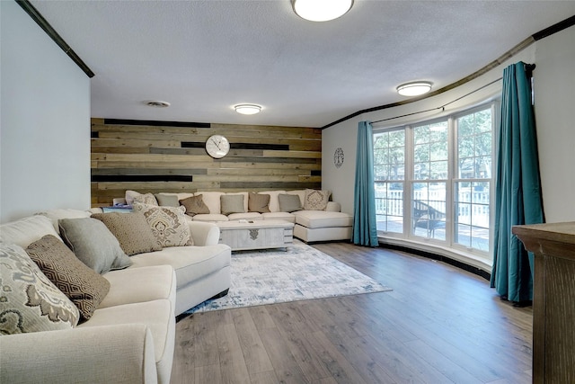 living room featuring wood-type flooring, crown molding, a textured ceiling, and wood walls