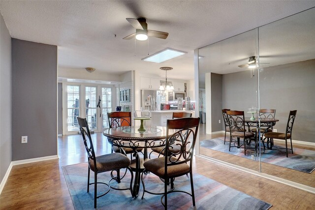 dining space with hardwood / wood-style floors, ceiling fan with notable chandelier, a textured ceiling, and a skylight