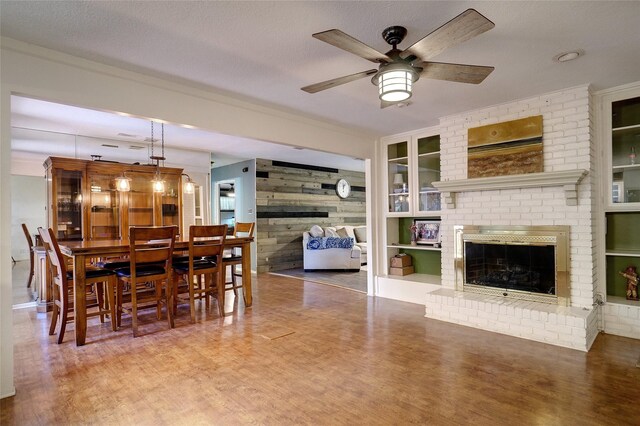 dining area with ceiling fan, built in features, a textured ceiling, wooden walls, and a fireplace