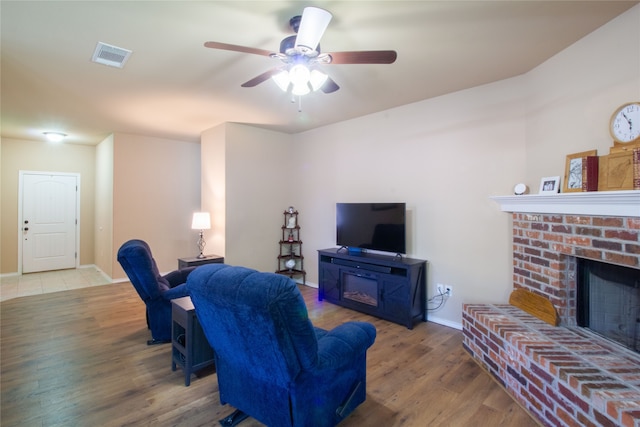 living room featuring ceiling fan, hardwood / wood-style floors, and a brick fireplace