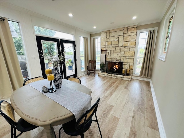dining space with crown molding, a stone fireplace, a wealth of natural light, and light hardwood / wood-style flooring