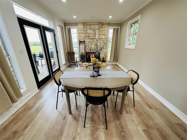 dining area with ornamental molding, a stone fireplace, and light hardwood / wood-style floors