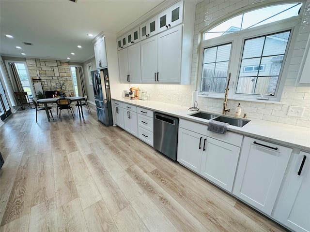 kitchen with white cabinetry, sink, fridge, stainless steel dishwasher, and light stone countertops