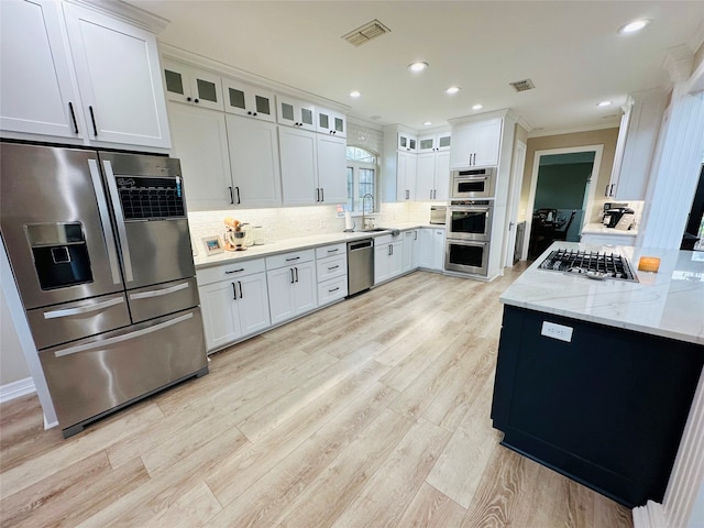 kitchen with light stone counters, white cabinets, stainless steel appliances, and light wood-type flooring