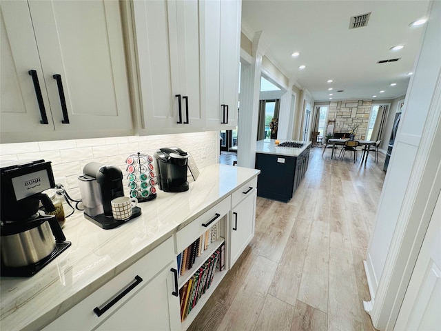 kitchen featuring stainless steel gas stovetop, white cabinets, crown molding, light stone countertops, and light hardwood / wood-style floors