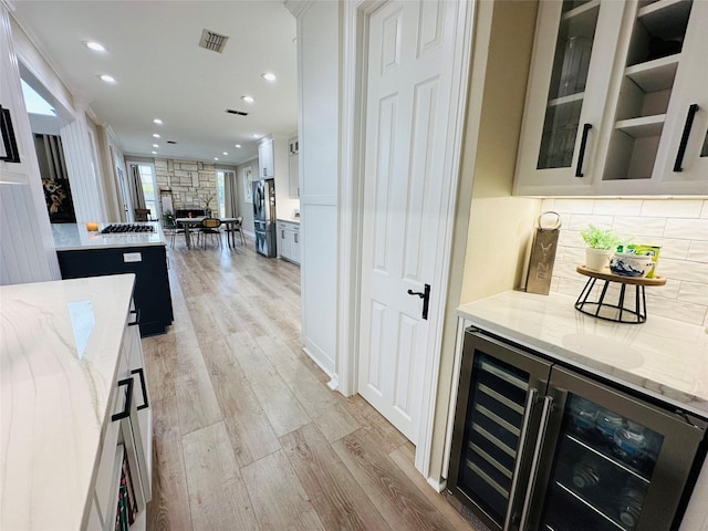 bar with stainless steel fridge, white cabinets, beverage cooler, light hardwood / wood-style floors, and light stone countertops