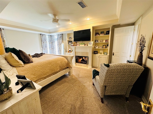 carpeted bedroom with ceiling fan, crown molding, a tile fireplace, and a tray ceiling