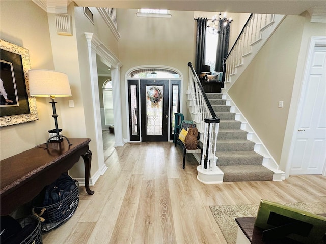 foyer with a towering ceiling, light hardwood / wood-style flooring, and decorative columns