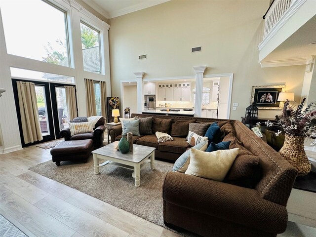 living room with decorative columns, a towering ceiling, light hardwood / wood-style floors, and ornamental molding