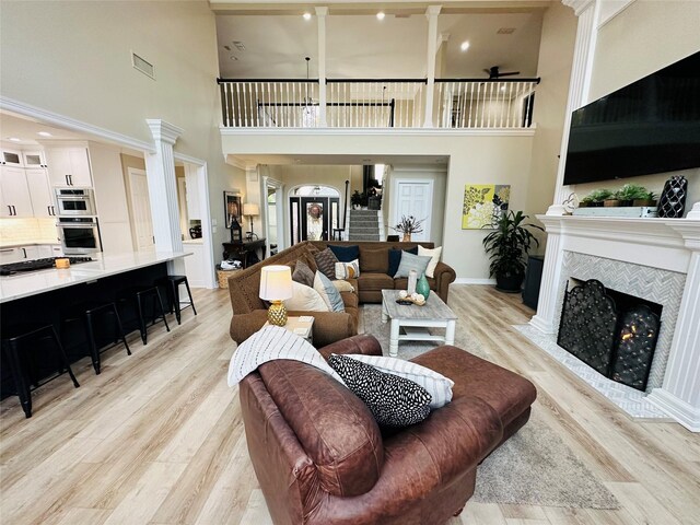 living room with a tile fireplace, a towering ceiling, and light wood-type flooring