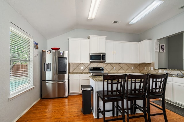 kitchen featuring a breakfast bar, lofted ceiling, dark wood-type flooring, white cabinets, and stainless steel appliances