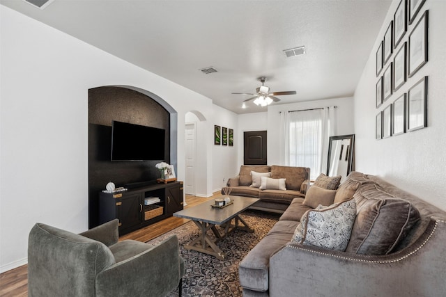 living room with dark wood-style floors, baseboards, visible vents, and ceiling fan