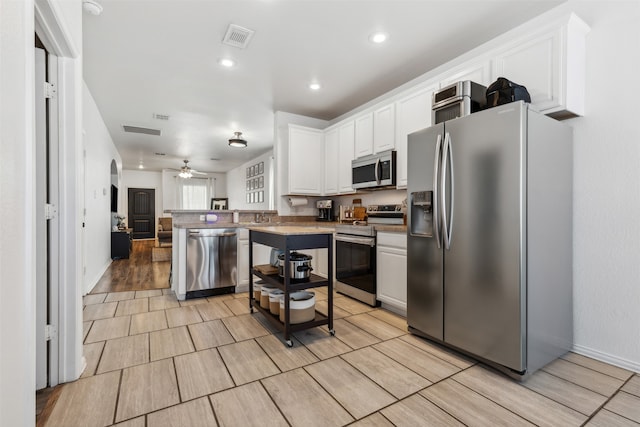 kitchen with ceiling fan, white cabinetry, a center island, light hardwood / wood-style flooring, and appliances with stainless steel finishes