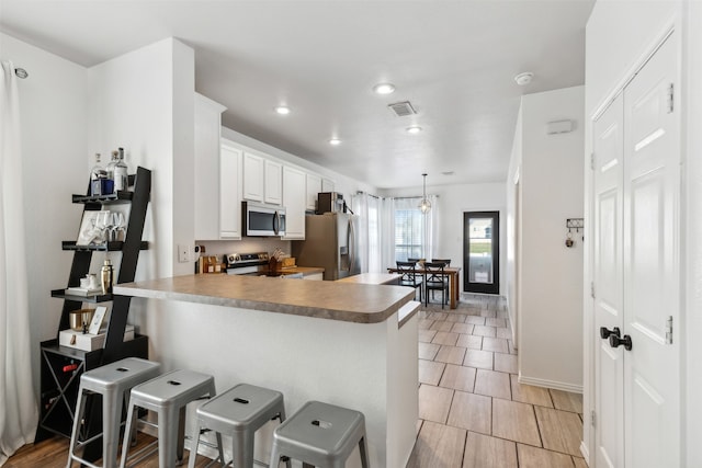 kitchen with kitchen peninsula, appliances with stainless steel finishes, a kitchen breakfast bar, pendant lighting, and white cabinets