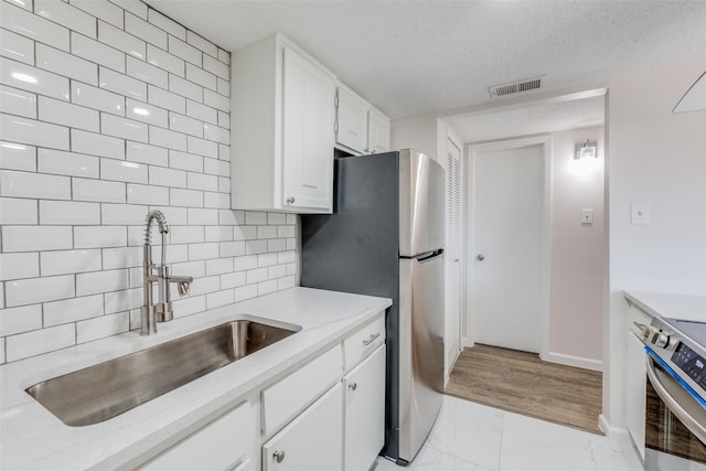 kitchen with white cabinetry, sink, tasteful backsplash, stainless steel fridge, and stove