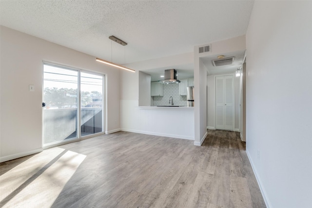 unfurnished living room with a textured ceiling, sink, and light hardwood / wood-style flooring