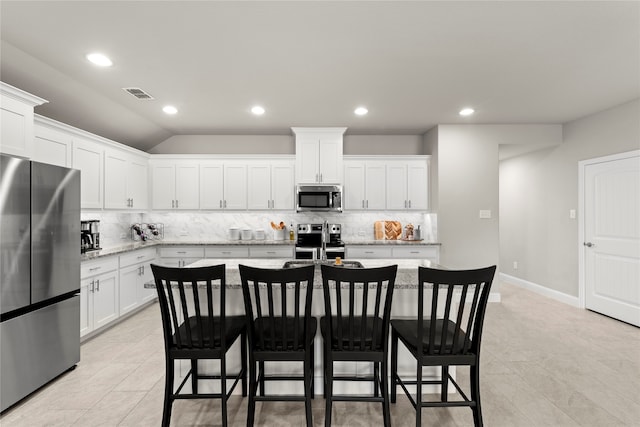 kitchen featuring white cabinetry, stainless steel appliances, light stone counters, backsplash, and an island with sink