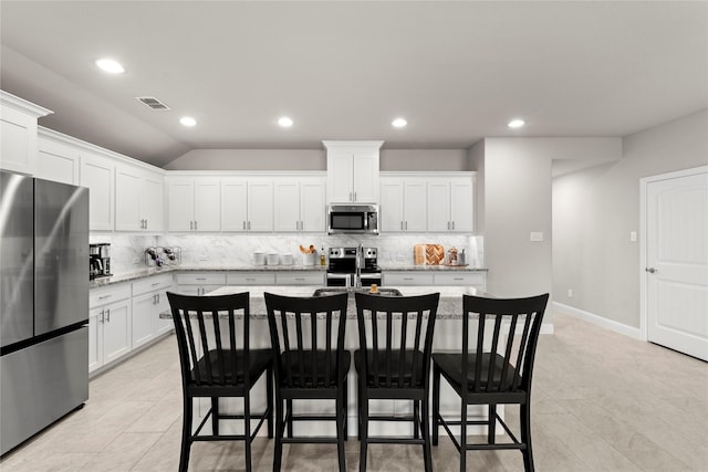 kitchen with a breakfast bar area, light stone counters, appliances with stainless steel finishes, a kitchen island with sink, and white cabinets