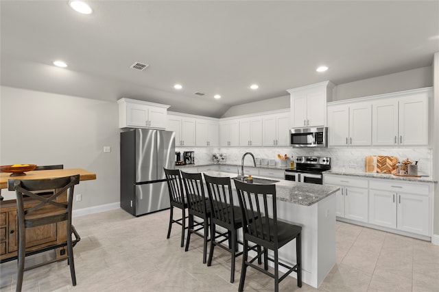 kitchen featuring decorative backsplash, white cabinetry, a kitchen island with sink, and appliances with stainless steel finishes