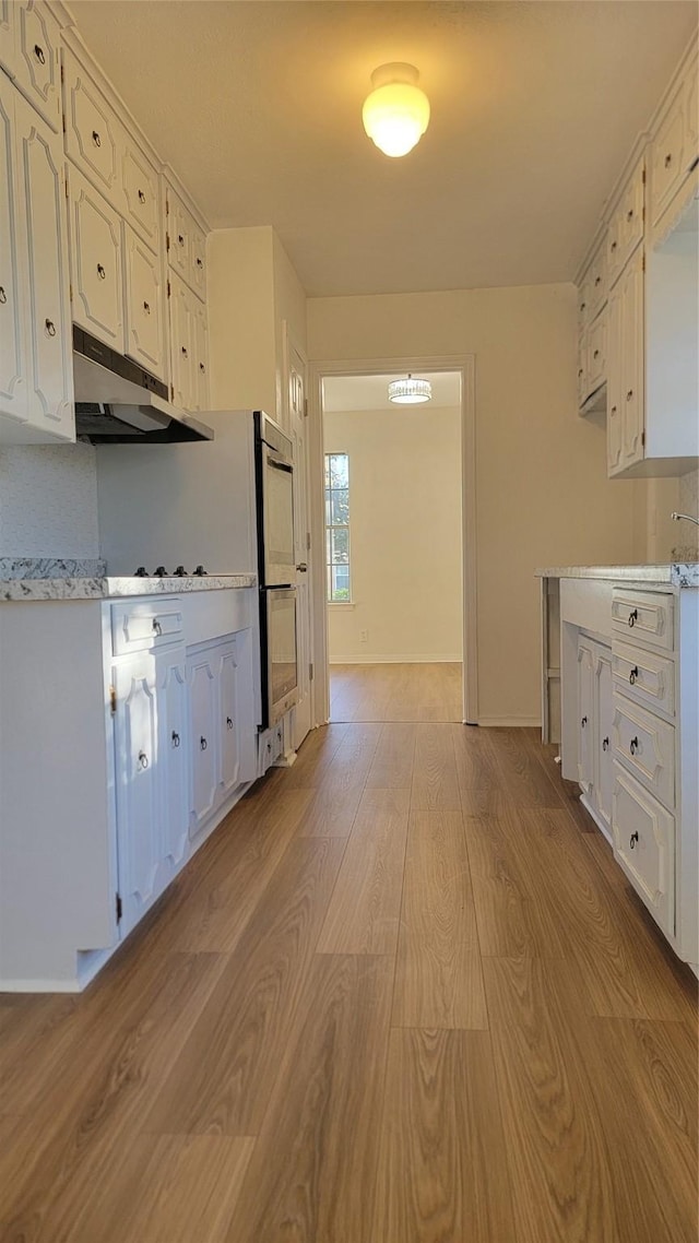 2001 Alma, Sherman, TX 75090 - kitchen featuring light wood-style floors, under cabinet range hood, light countertops, multiple ovens, and white cabinetry