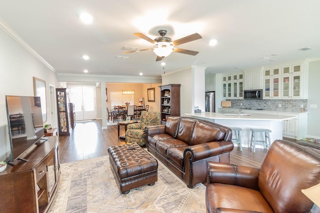 living room with light wood finished floors, visible vents, and crown molding