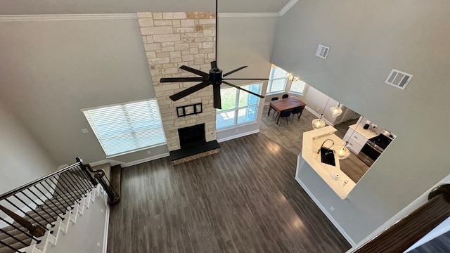 unfurnished living room with a towering ceiling, ornamental molding, ceiling fan, dark hardwood / wood-style floors, and a stone fireplace