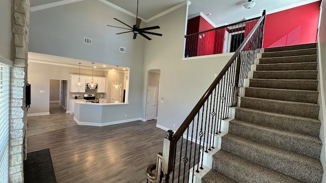 staircase with hardwood / wood-style floors, high vaulted ceiling, ceiling fan with notable chandelier, ornamental molding, and a fireplace