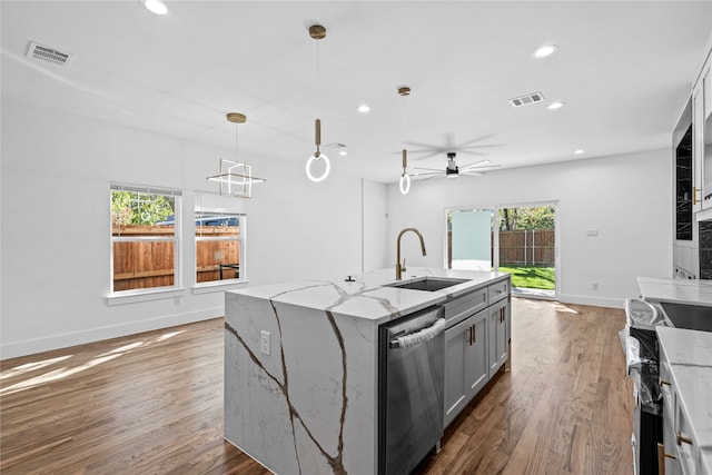 kitchen with light stone counters, sink, dishwasher, plenty of natural light, and an island with sink