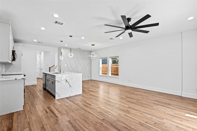 kitchen featuring ceiling fan, an island with sink, pendant lighting, white cabinets, and light wood-type flooring