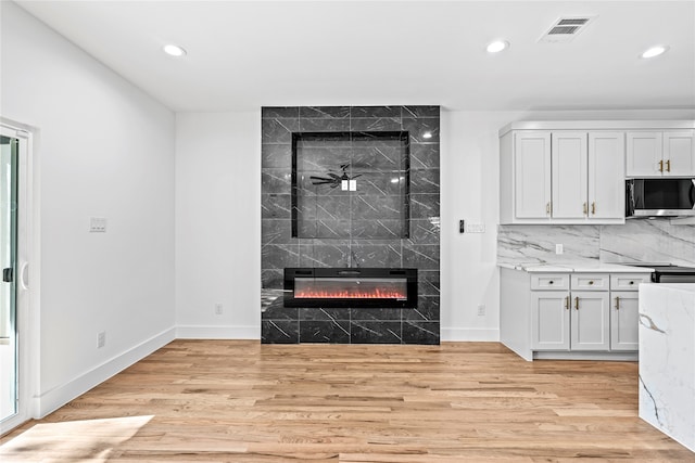 interior space with light stone countertops, ceiling fan, a tile fireplace, light hardwood / wood-style flooring, and white cabinets