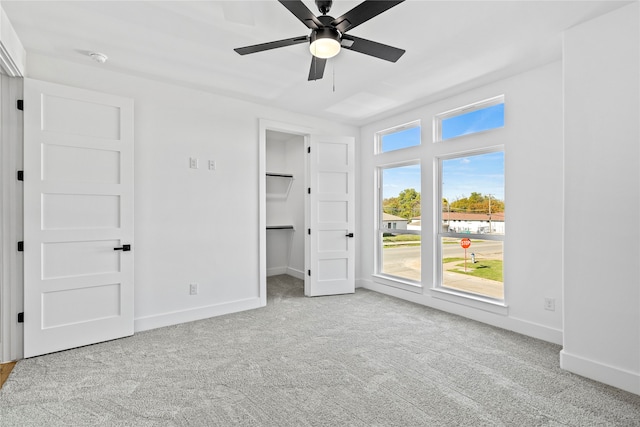 unfurnished bedroom featuring a walk in closet, ceiling fan, and light colored carpet