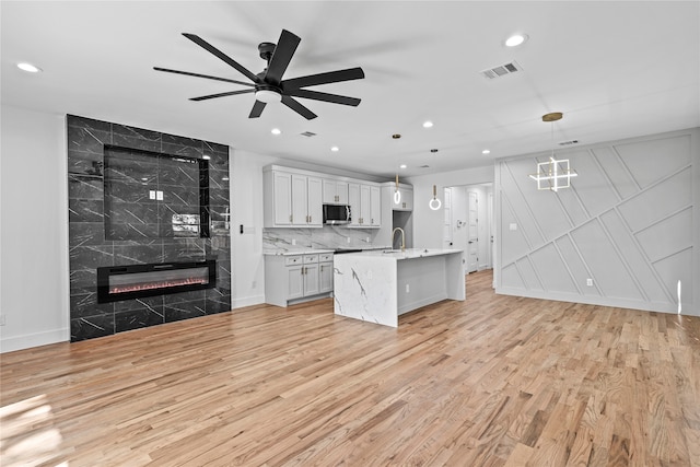 kitchen with a tile fireplace, white cabinetry, light hardwood / wood-style flooring, pendant lighting, and a kitchen island with sink