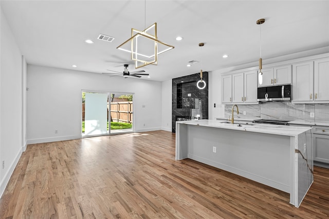 kitchen featuring a kitchen island with sink, hanging light fixtures, light stone countertops, appliances with stainless steel finishes, and light hardwood / wood-style floors