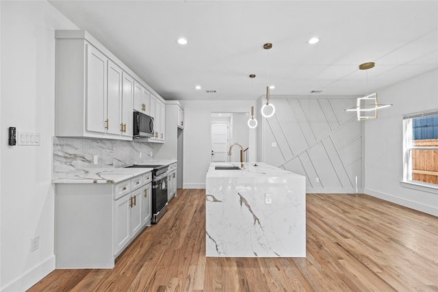 kitchen featuring pendant lighting, white cabinets, light hardwood / wood-style flooring, light stone counters, and stainless steel appliances